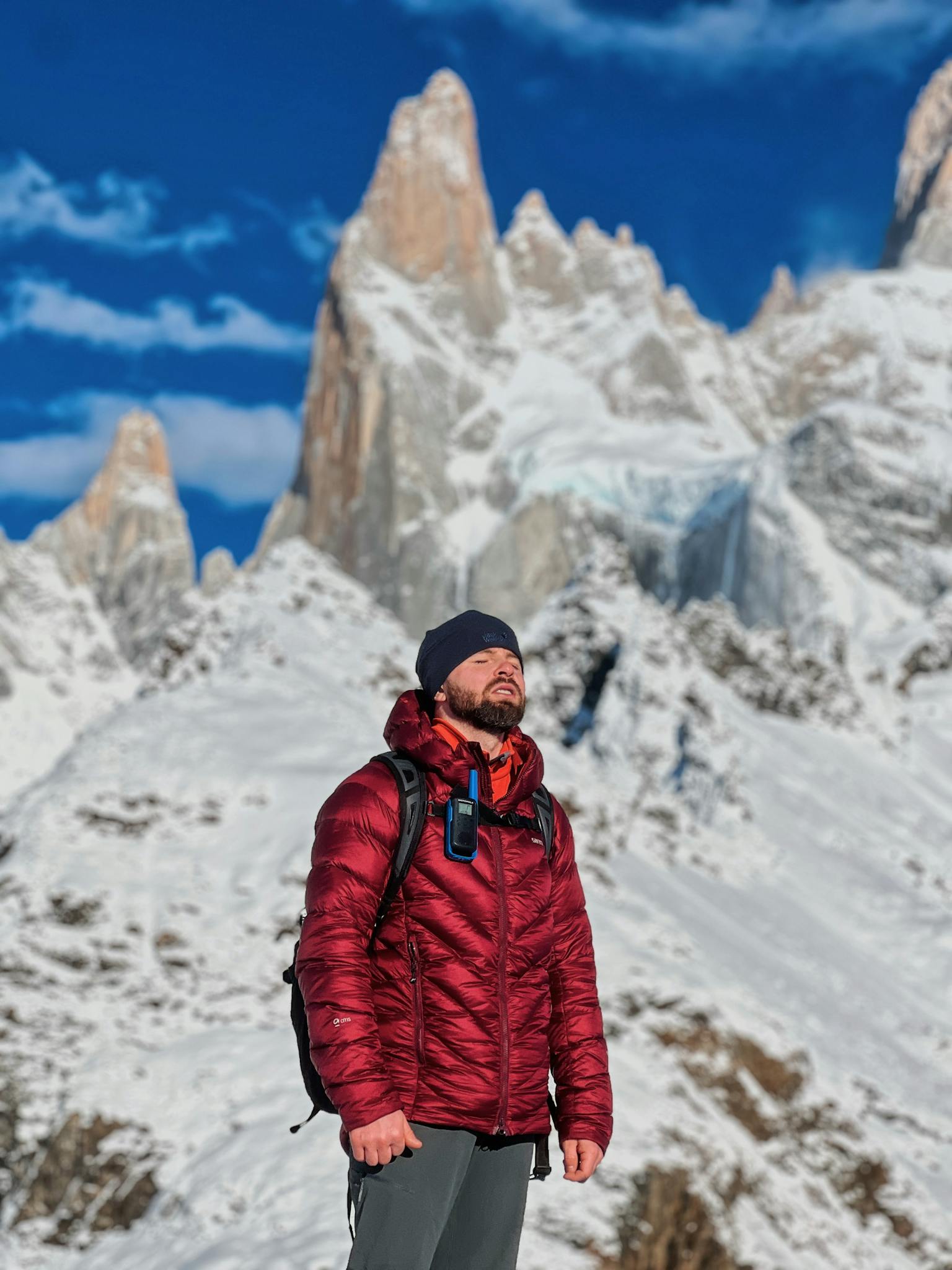 Man in a red jacket standing on a snowy mountain under a clear blue sky, showcasing adventure.